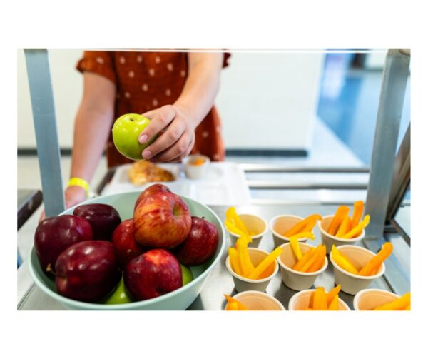 A person selects a green apple from a display of fresh fruit in a school setting