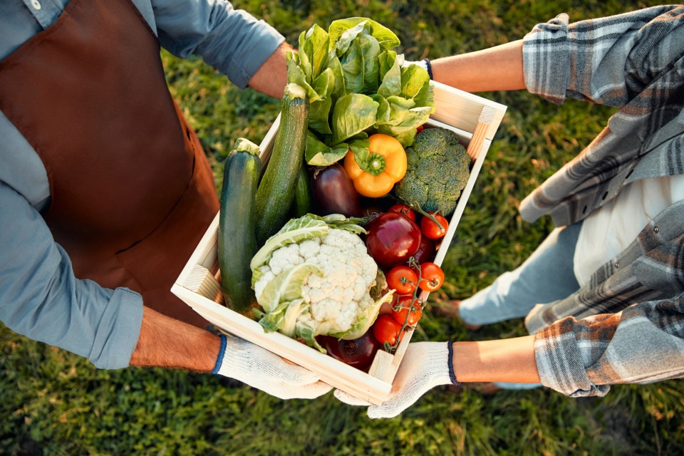 Two adults exchange a crate of fresh vegetables