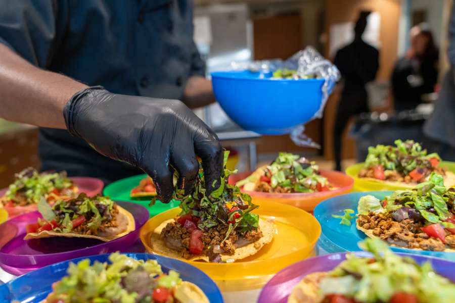 A chef adds shredded lettuce to a tostada being prepared for lunch at a community institution