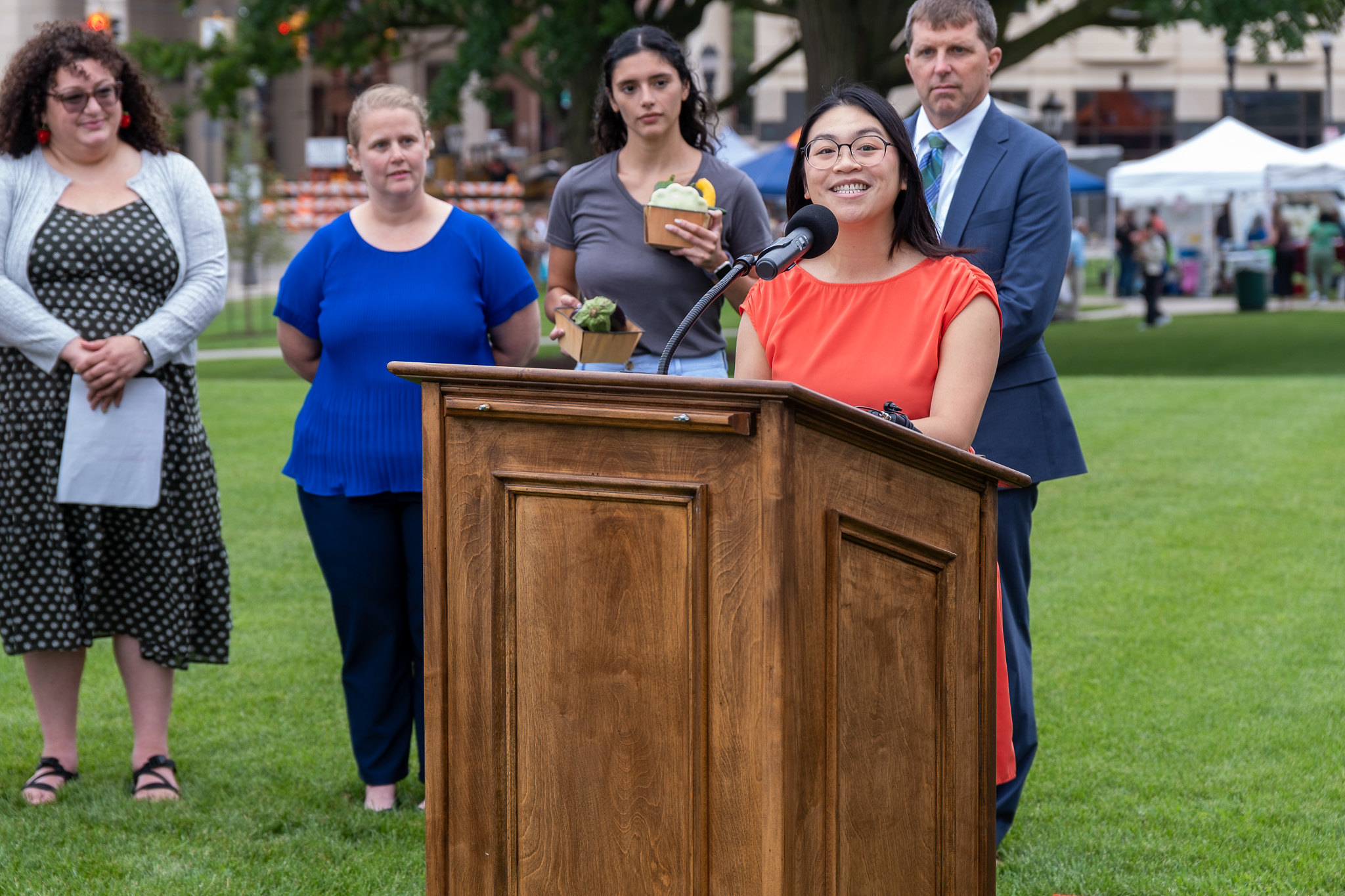 Melanie Wong Tran speaks from a podium at the Michigan State Capitol Farmers Market