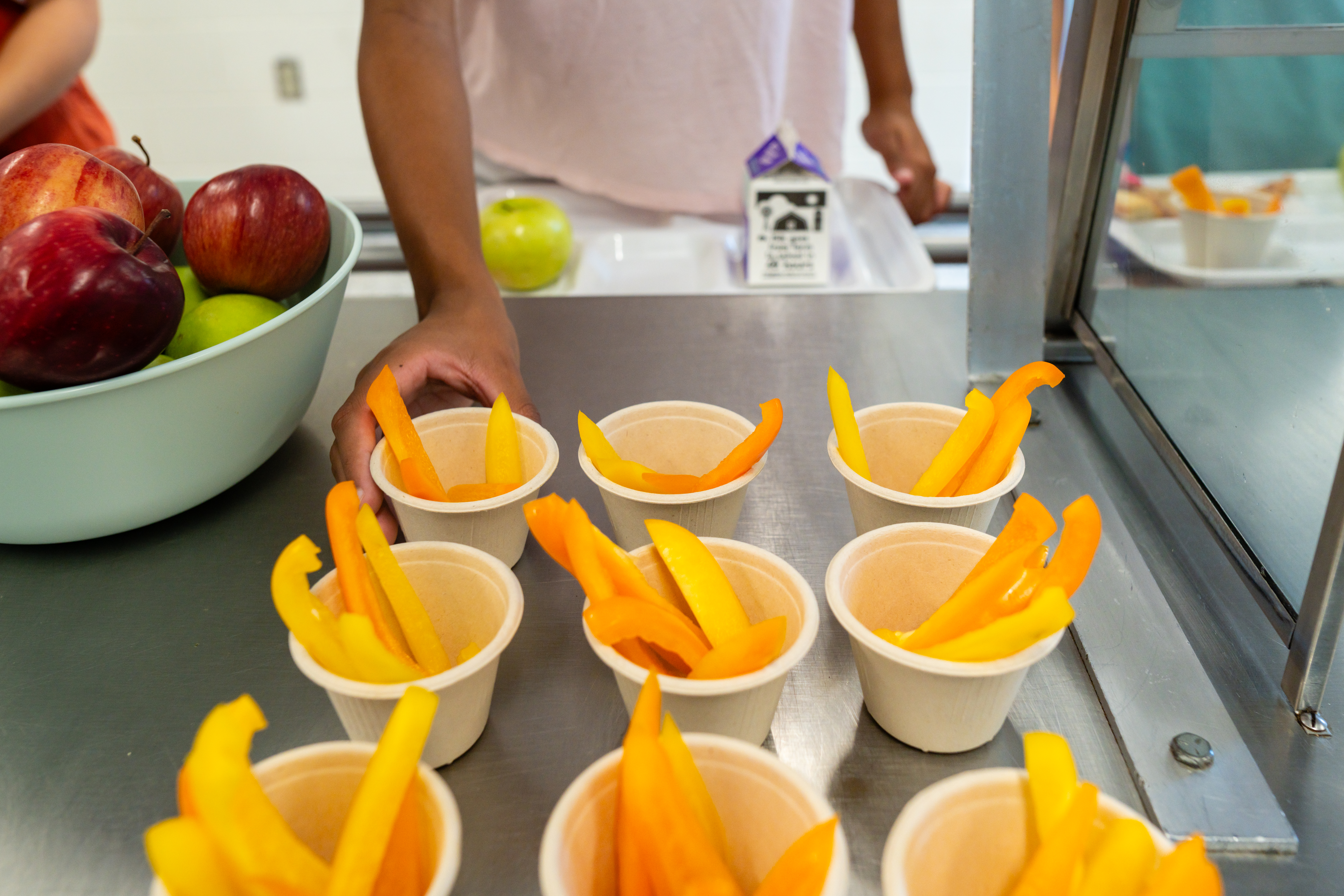 A child selects a cup of cut fresh yellow pepper strips from a cafeteria serving line