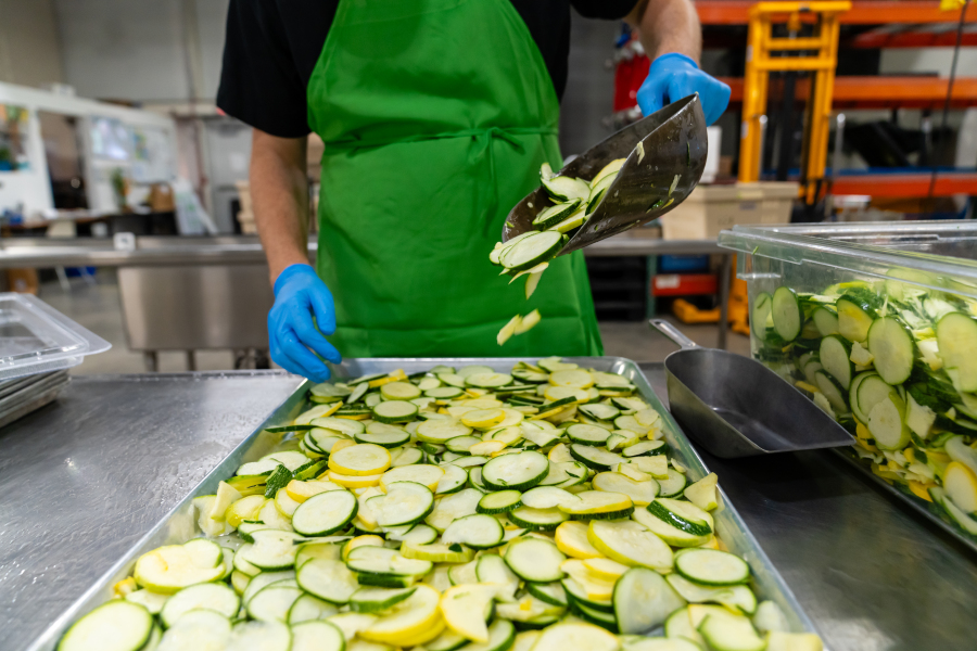 An institutional food service worker prepares round slices of fresh zucchini