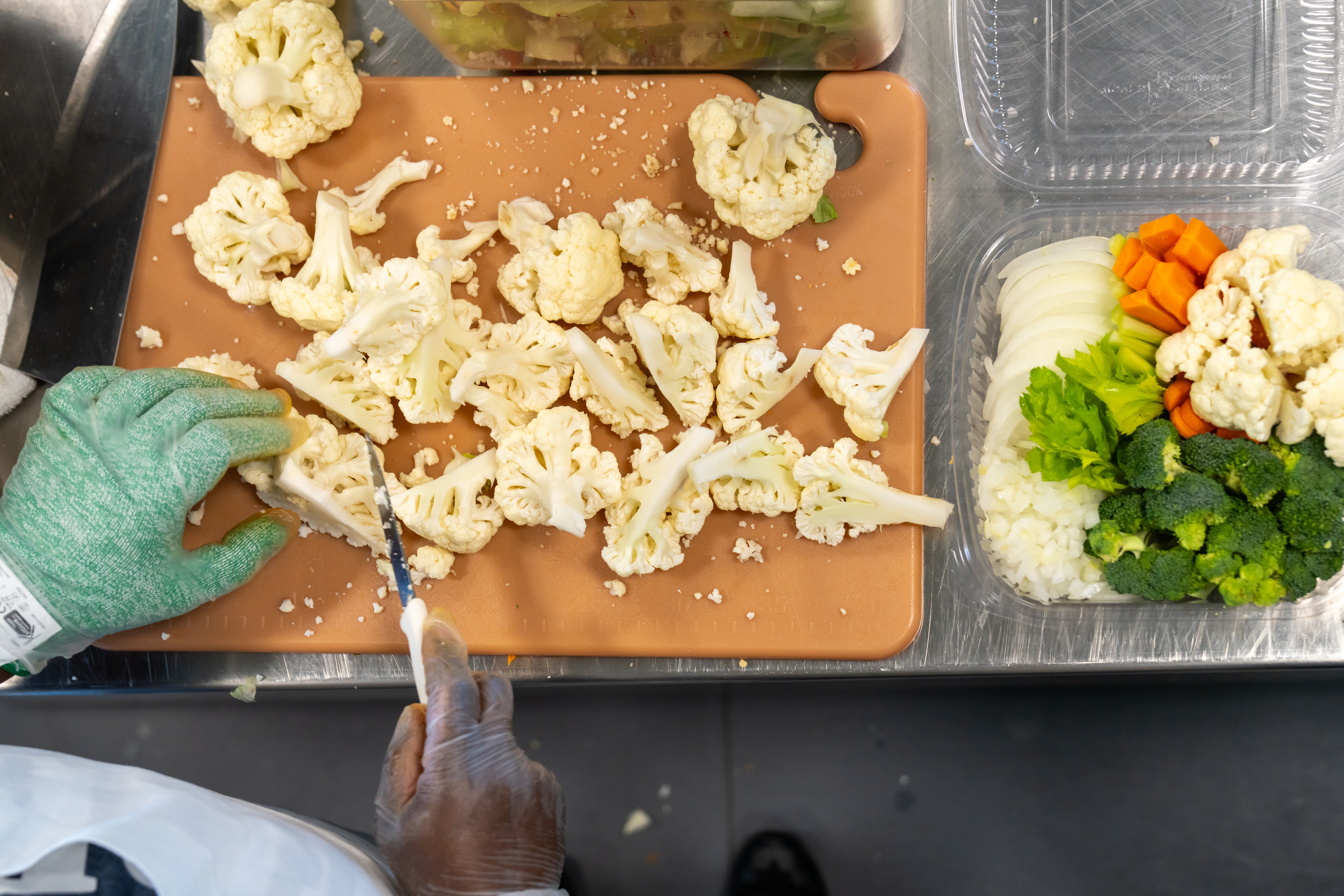 An institutional food worker cuts fresh cauliflower