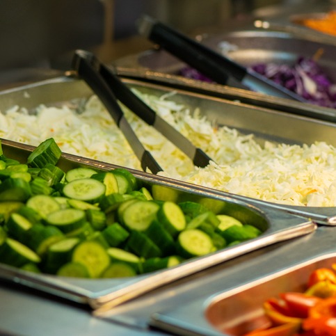 Cucumbers and shredded cheese are offered in silver school lunch serving trays
